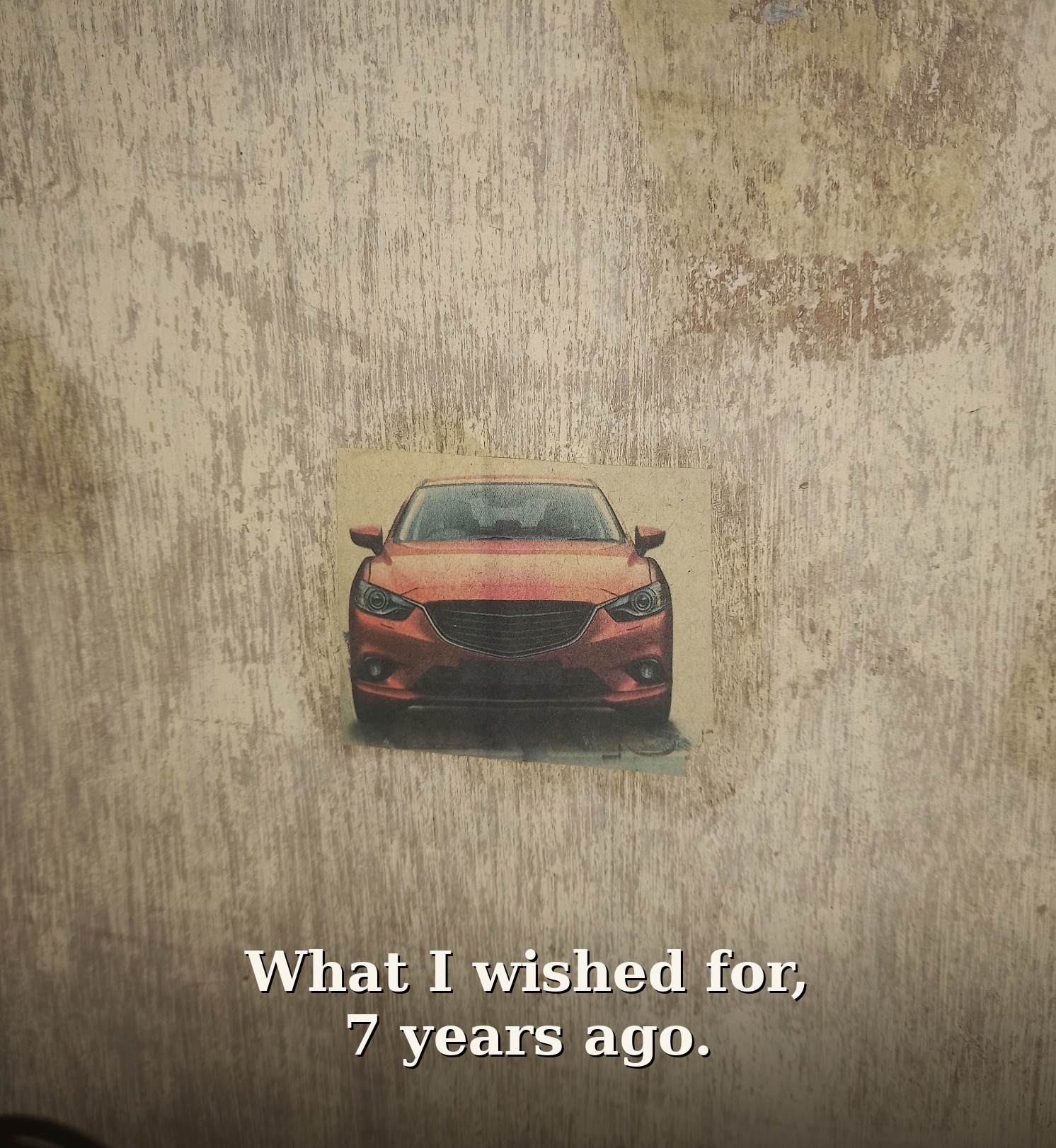 Newspaper cutout photo of a red Mazda with the words 'What I wished for, 7 years ago' printed over it